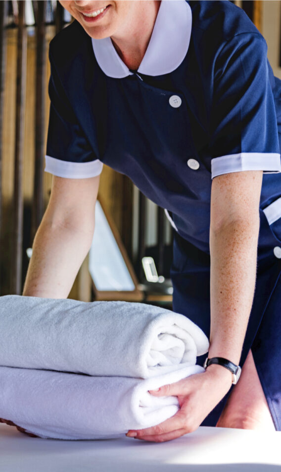 A person in uniform putting clean towels down on the bed