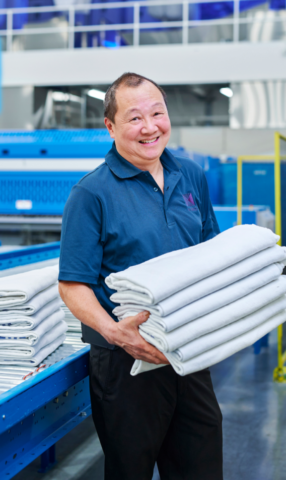 A happy K-Bro employee holding clean and pressed hospital blankets